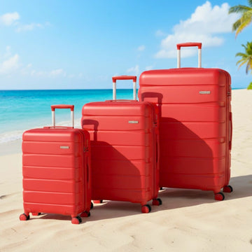 Three red suitcases of different sizes on a sandy beach with ocean and sky in the background