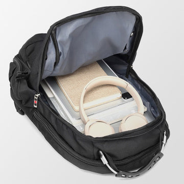 Black backpack with a compartment containing books and beige headphones on a light gray background